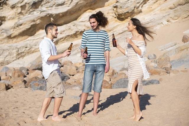 Imagen de dos chicos y una chica tomando cerveza en una playa