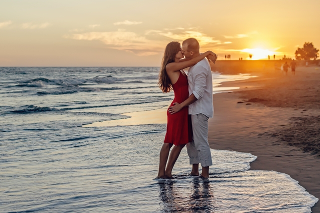 Imagen de una pareja que se besa en la orilla del mar y ante una puesta de sol