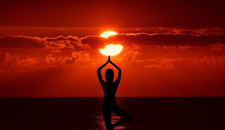 Imagen de una practicante de yoga frente al sol en la playa durante el amanecer